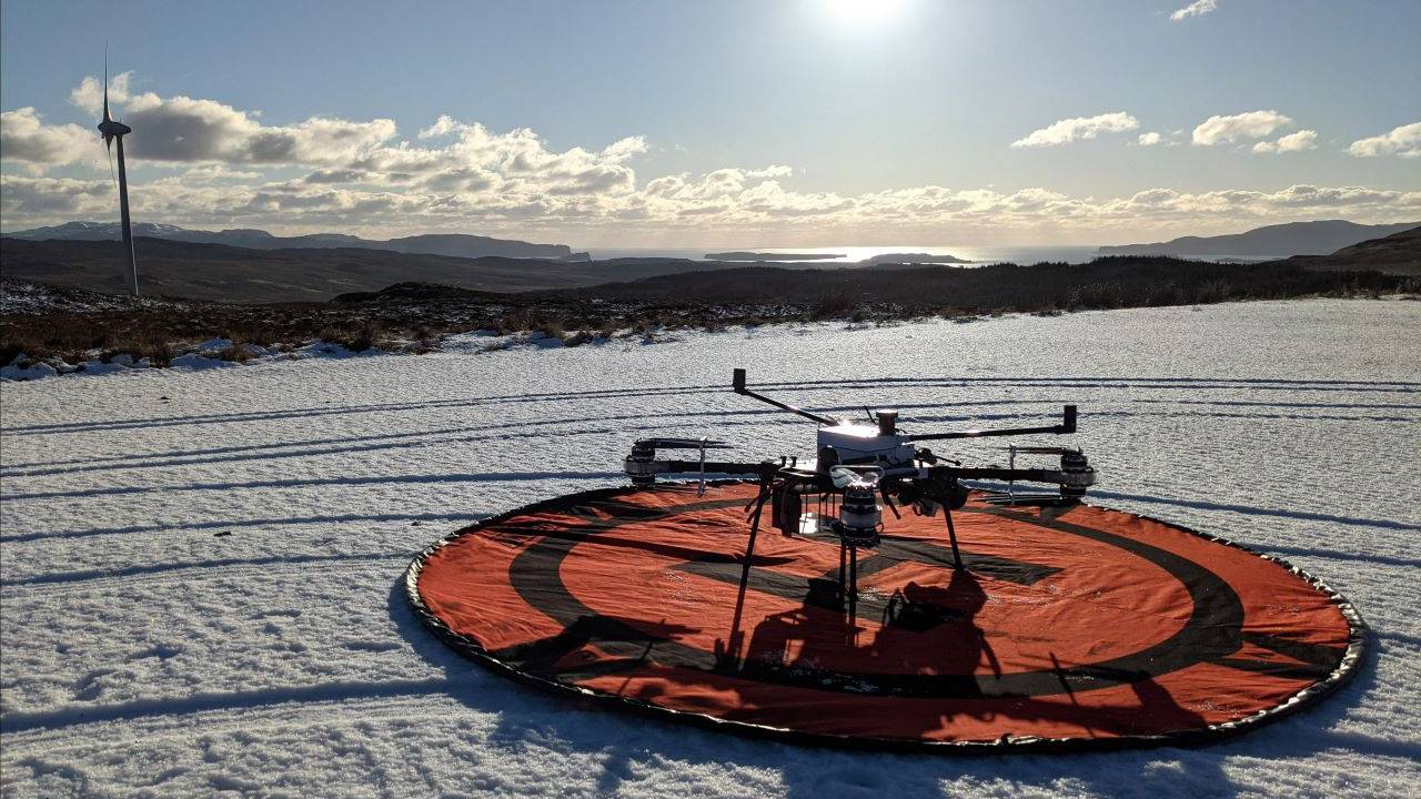 This image is of our drone on a snow covered ground at the start of an inspection. There is a wind turbine in the far distance.