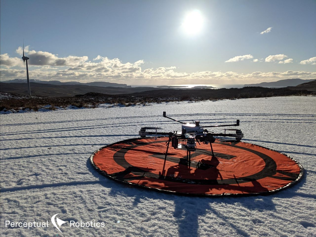This image is of our drone on a snow covered ground at the start of an inspection. There is a wind turbine in the far distance.