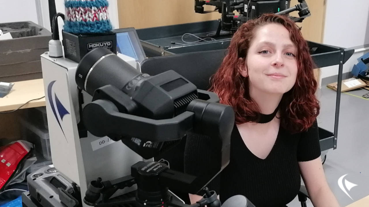 This is an image of Estilla at her desk in the office. One of our drones is on the table next to her.